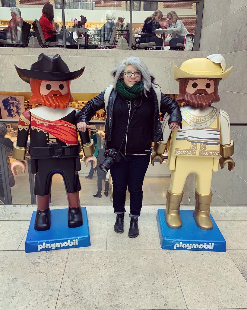 A short woman stands next to some Playmobil statues that are the same height as she is