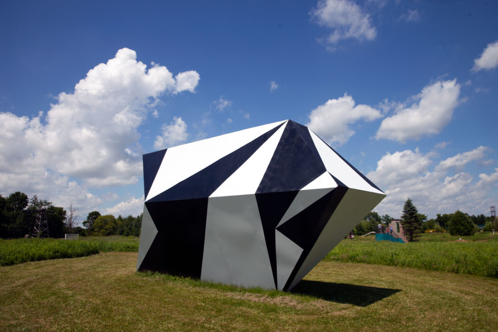Large black and white abstract sculpture outdoors, in a field