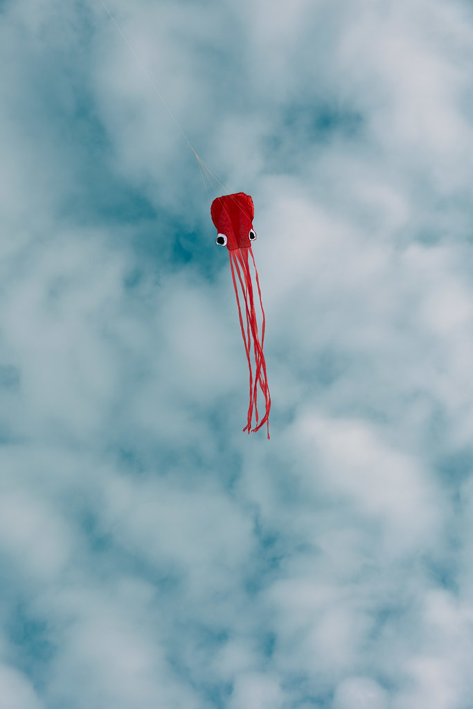 A red octopus kite flying against a cloudy sky