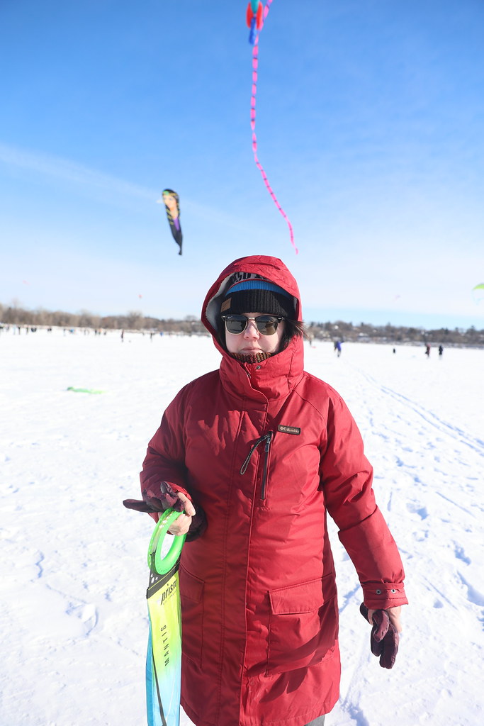 A woman bundled up on a frozen lake with kites flying behind her