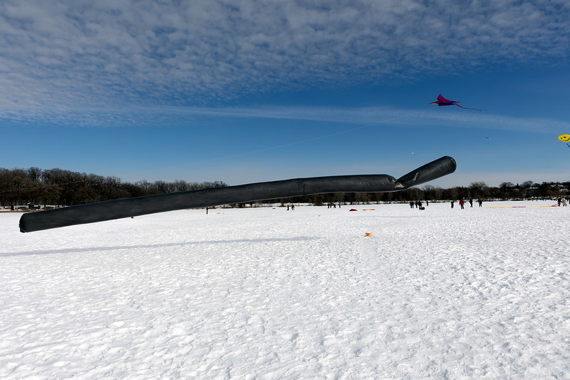 Kite that is a long tube of black material hovering just above a frozen lake