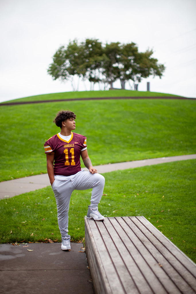 A young man in a football uniform posing in a park with one foot on a bench