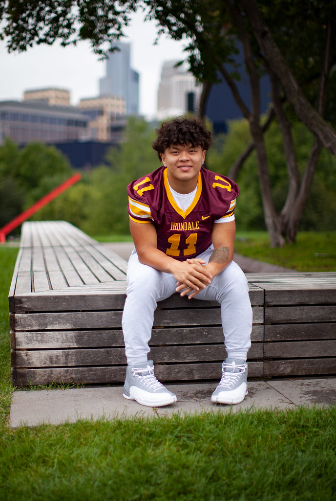 A young man in a football uniform sitting on a bench in a park