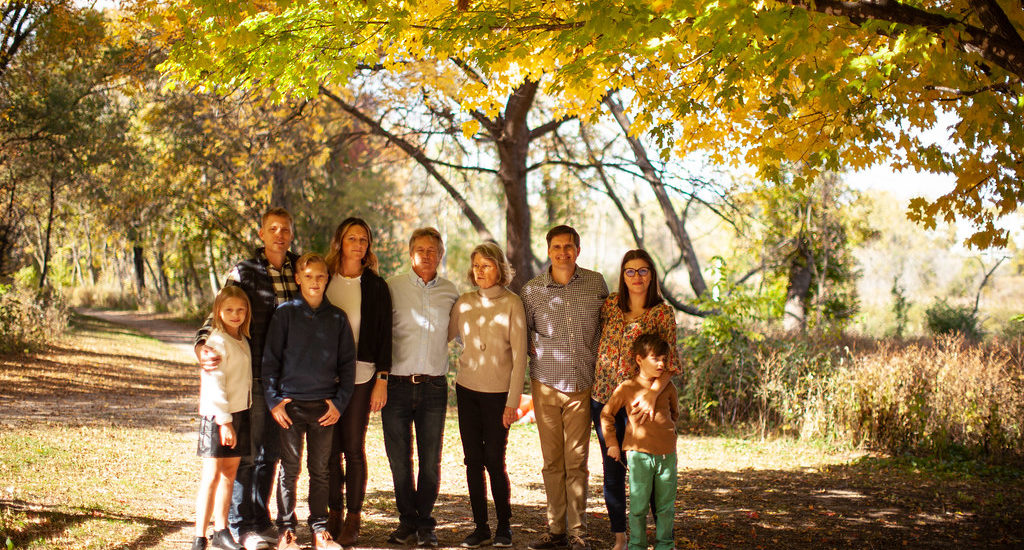 Group shot of three generations of a family standing under a tree in full Fall colors