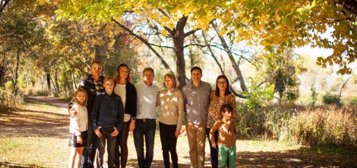Group shot of three generations of a family standing under a tree in full Fall colors